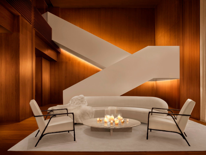 The lobby of The Tokyo Edition, Ginza, with a zig-zagging white staircase leading down to a curved long white sofa and two white chairs, on a white rug