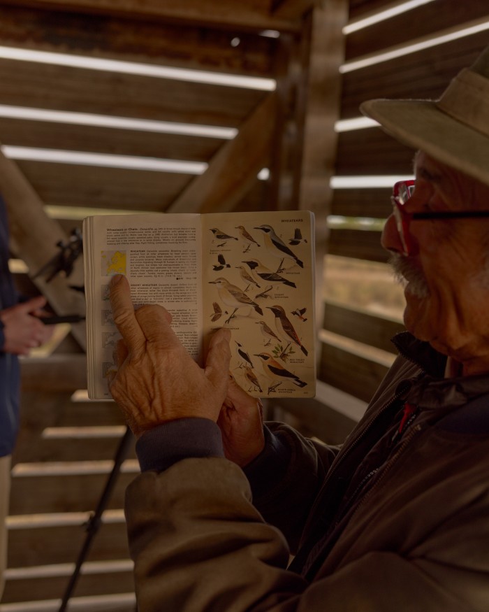 An ornithologist shows guests pictures of birds in a guide book in a bird-watching hut