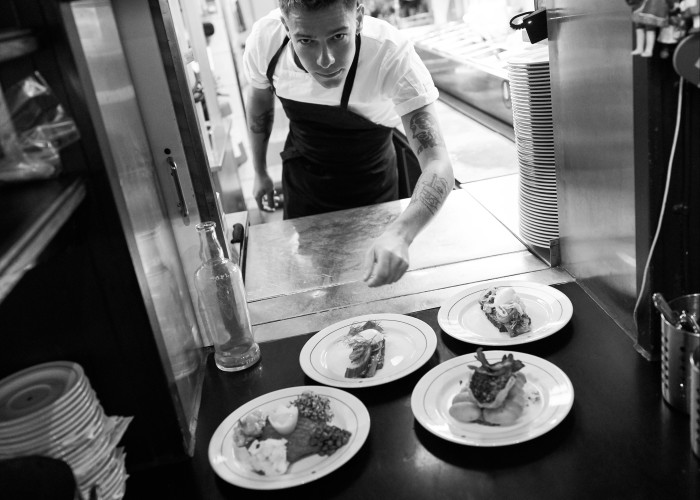 A black and white image of Schønnemann chef Oscar Ptak Fréder in front of five plates of food, one of which is a steak tartare