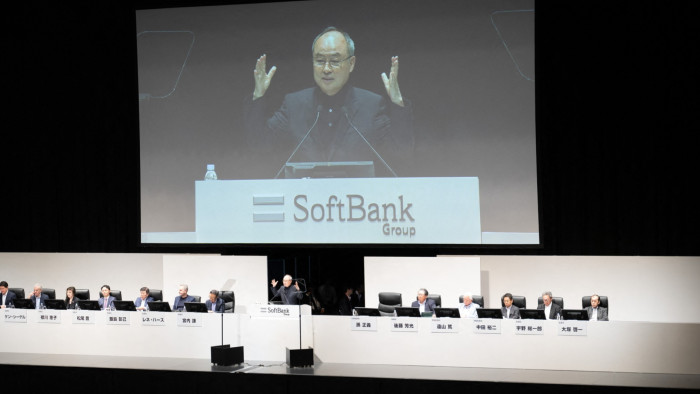 Masayoshi Son speaks onstage at the annual shareholders’ meeting, with executives seated on either side of him