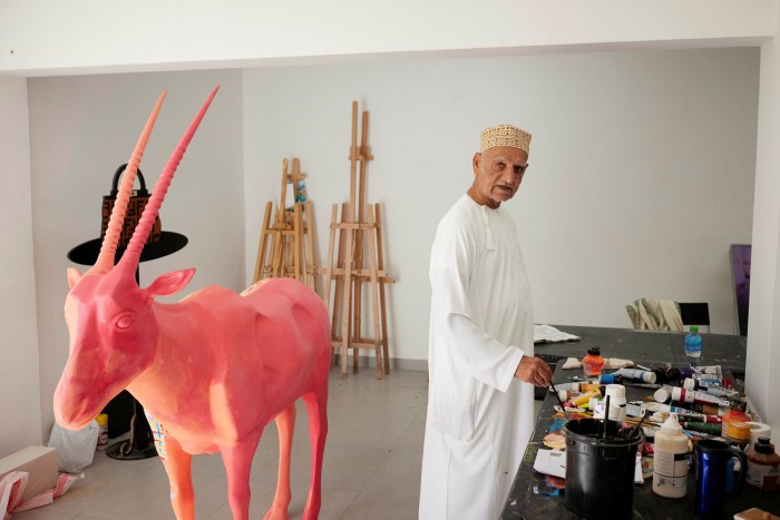 A man in a long white thawb tunic looking cautiously at the camera next to a large painted pink goat