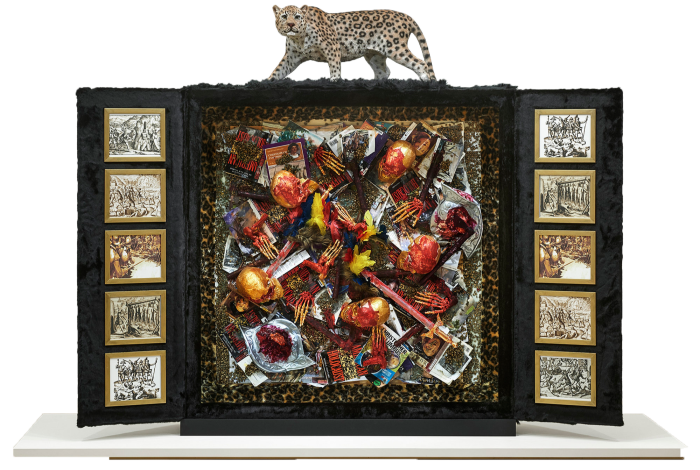 A freestanding cabinet open to reveal small skeletons covered in blood, with a tiger on top