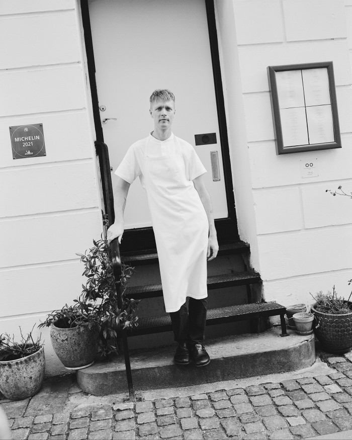 A black and white image of chef Magnus Pettersson of Selma standing on steps at the restaurant’s entrance 