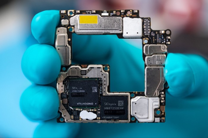 A hand in a turquoise latex glove holds the working components of the Mate X5 smartphone 