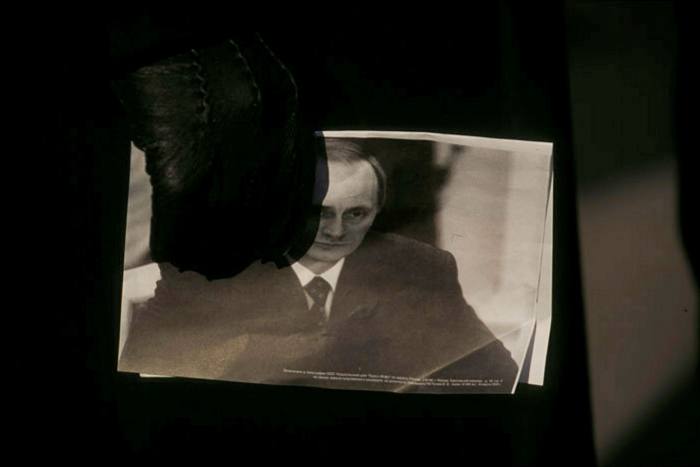 A person’s gloved hand holds a picture of Vladimir Putin