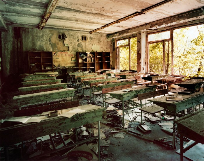 A classroom is recognisable but totally wrecked. Pale light comes through a window