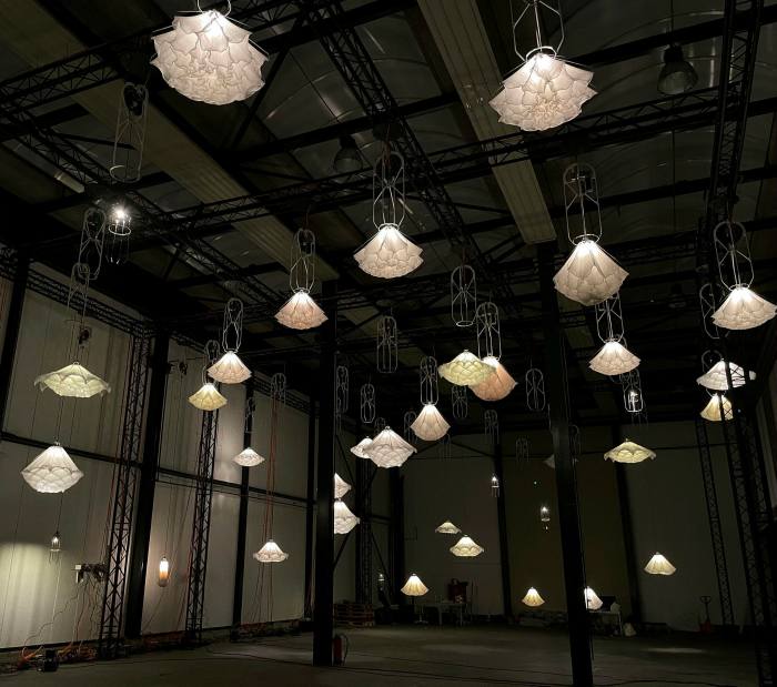 Many elaborate white lampshades hang from a dark ceiling