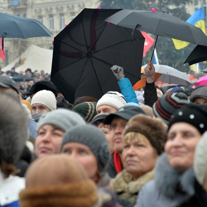 A crowd of people march through the streets carrying umbrellas