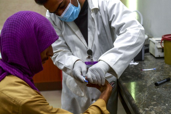 In this picture taken on March 26, 2021, a laboratory technician takes a blood sample from a man for an HIV test at a HIV treatment support centre in Rato Dero, in southern Sindh province