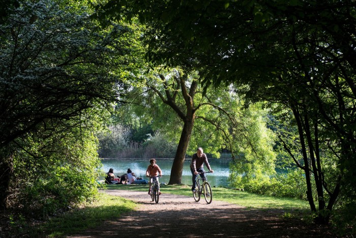 Cyclists on a tree-lined path by a lake in Boscoincittà public park