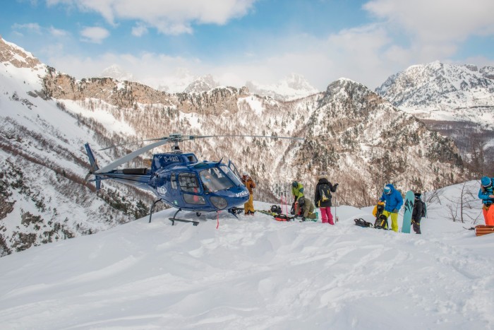 A group of skiers standing on the snow-covered ground next to a helicopter, mountain slopes behind