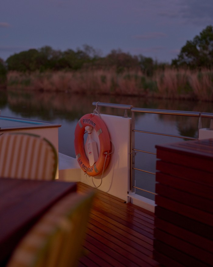 The wooden deck of a barge sailing along a waterway at dusk