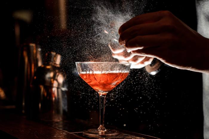 Bartender’s hands sprinkling juice into a cocktail glass filled with alcoholic drink