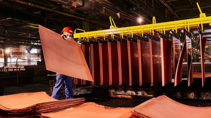 A worker handles newly formed copper cathode sheets in a warehouse