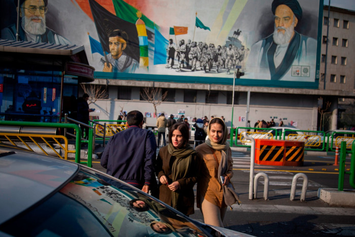 A pair of Iranian women pass a mural in Tehran displaying the present and former supreme leader