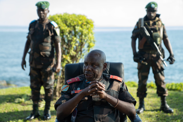 Maj Gen Peter Cirimwami sits in a chair flanked by FARDC soldiers