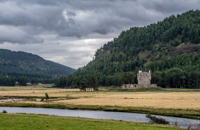 The 17th-century Braemar Castle, with forested hills behind it and a river running across the foreground