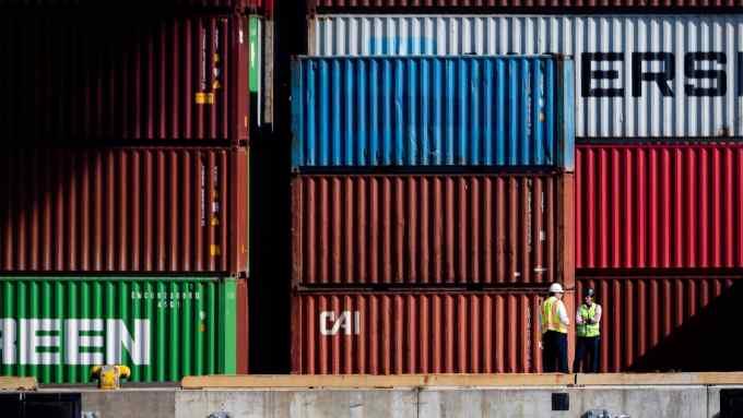 Two dock workers talk next to stacked containers at the Port of Baltimore