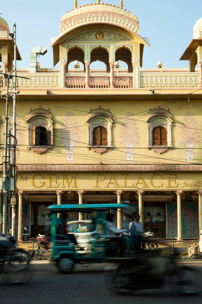 The yellow columned exterior of The Gem Palace, with a tuk tuk passing in front