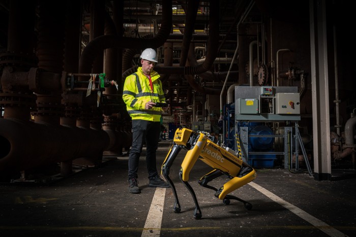 Man in hi-vis jacket next to a yellow robot dog in a power plant