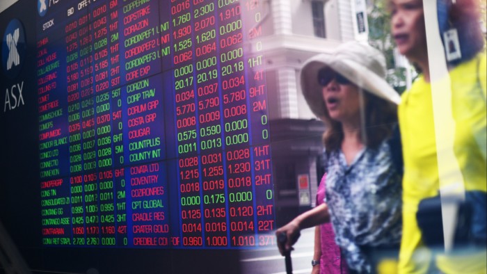 Passers-by next to market trading boards at the Australian Securities Exchange in Sydney
