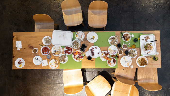 A dining table, viewed from above, and littered with cutlery, napkins, glasses and plates of unfinished food
