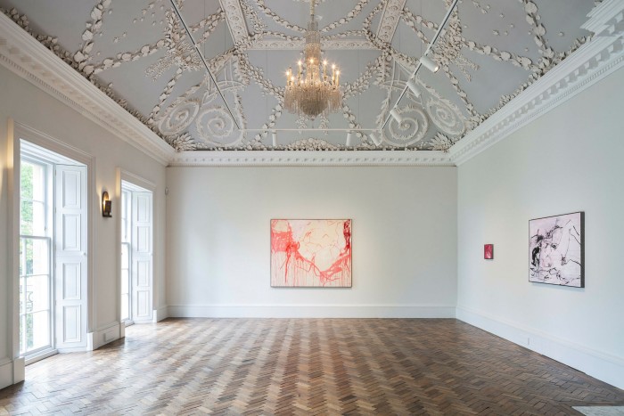 A red dribbling canvas and a pink dribbling canvas are on the walls of a grand pale ballroom complete with chandelier