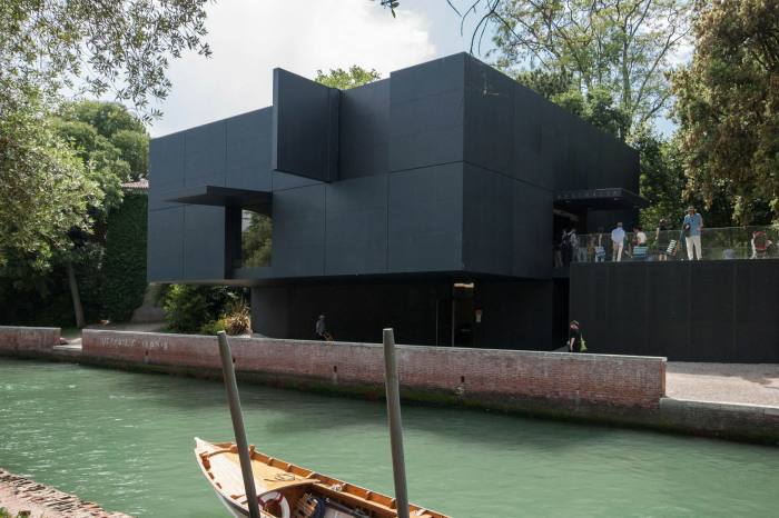 A two-storey building of black panels set by a canal