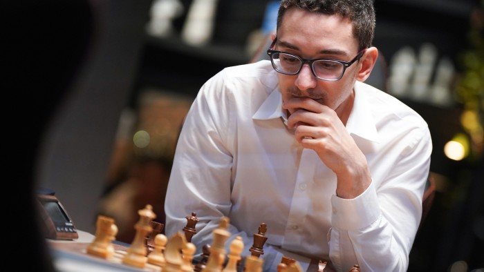 A man in glasses and white shirt leans over a chessboard