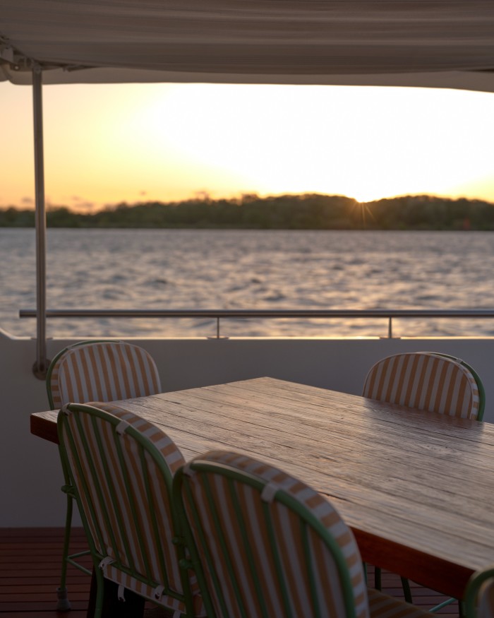 A table and chairs on the deck of the boat with a view of the sunset 