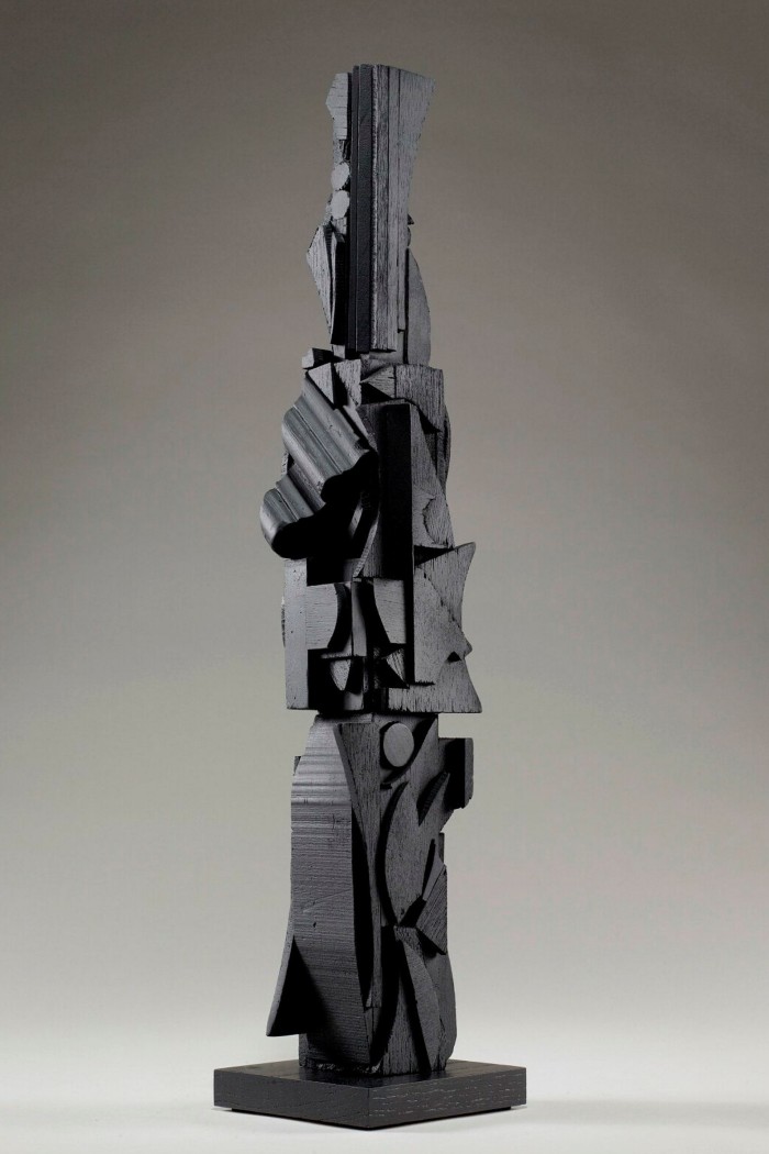 A tall thin black wooden sculpture made from abstract shapes