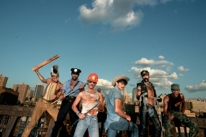 Six people stand on a roof top dressed, from left, as a Native American indian, policeman, construction worker, cowboy, biker and soldier
