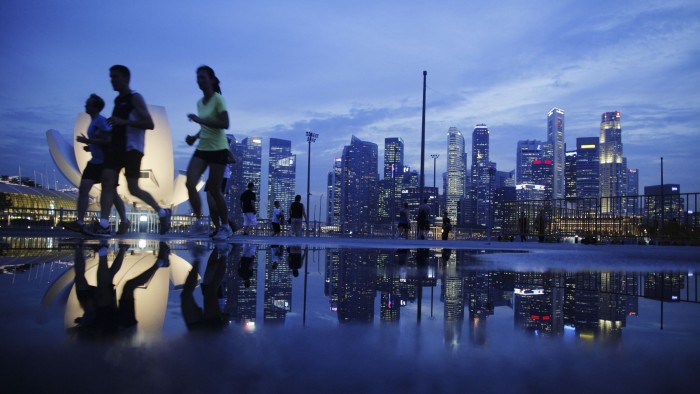 Joggers run in front of a view of the skyline of Singapore’s financial district