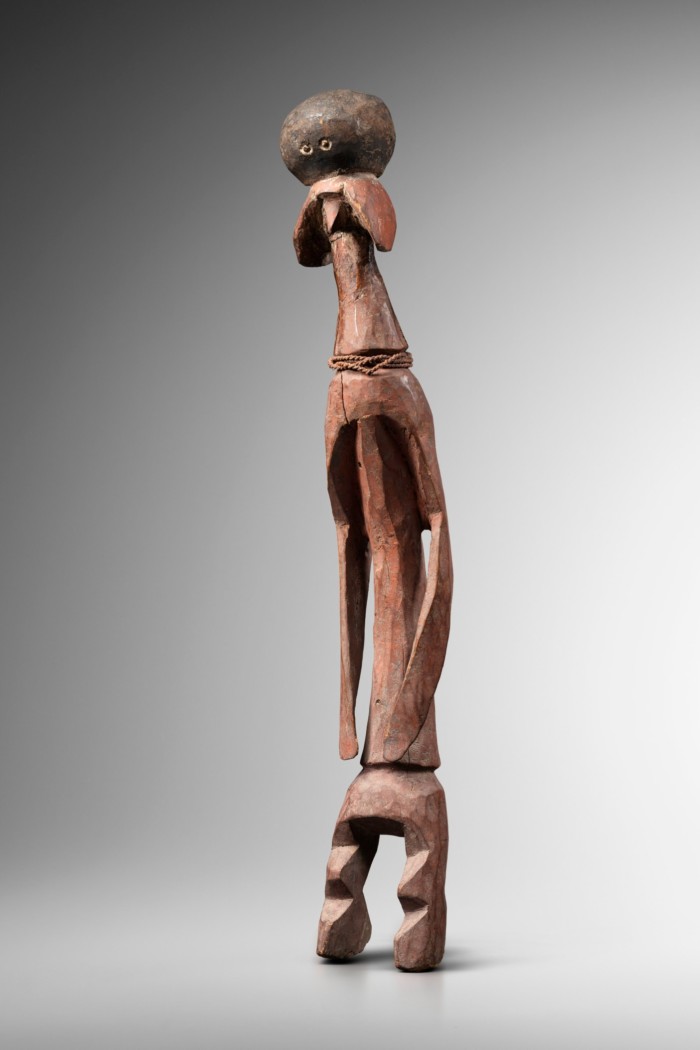 Tall thin wooden sculpture of a person with long arms and short legs