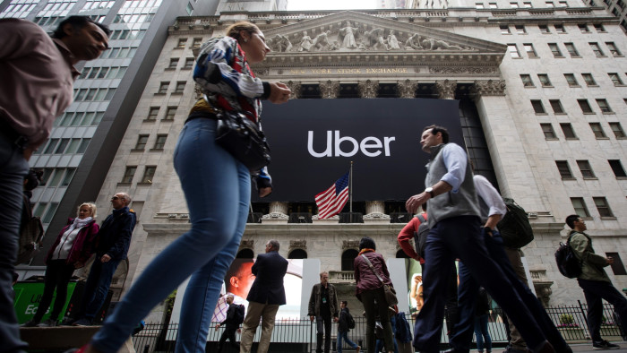Pedestrians pass in front of the New York Stock Exchange during Uber’s initial public offering on Friday, May 10, 2019