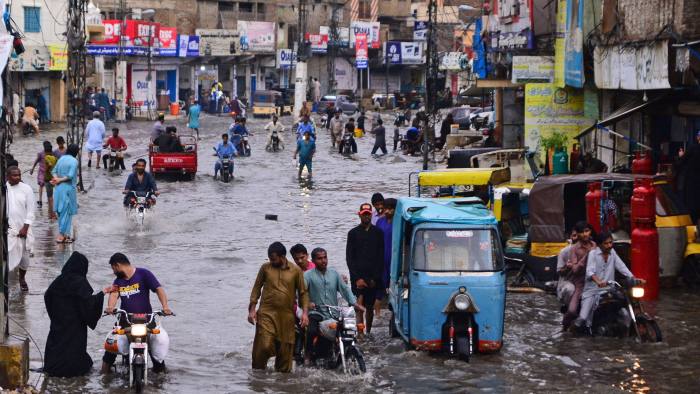 Commuters make their way through a flooded street during monsoon rainfall in Hyderabad