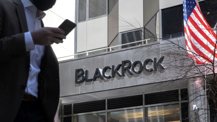 A pedestrian holding a smartphone passes in front of BlackRock headquarters in New York