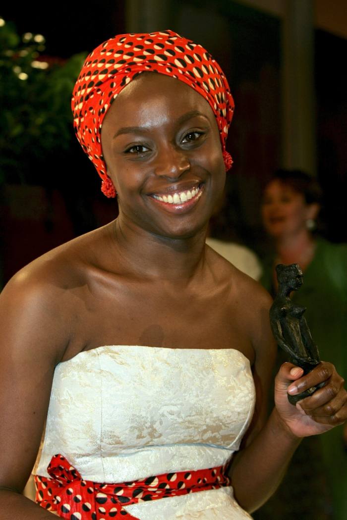 A smiling young woman in white strapless gown and red turban