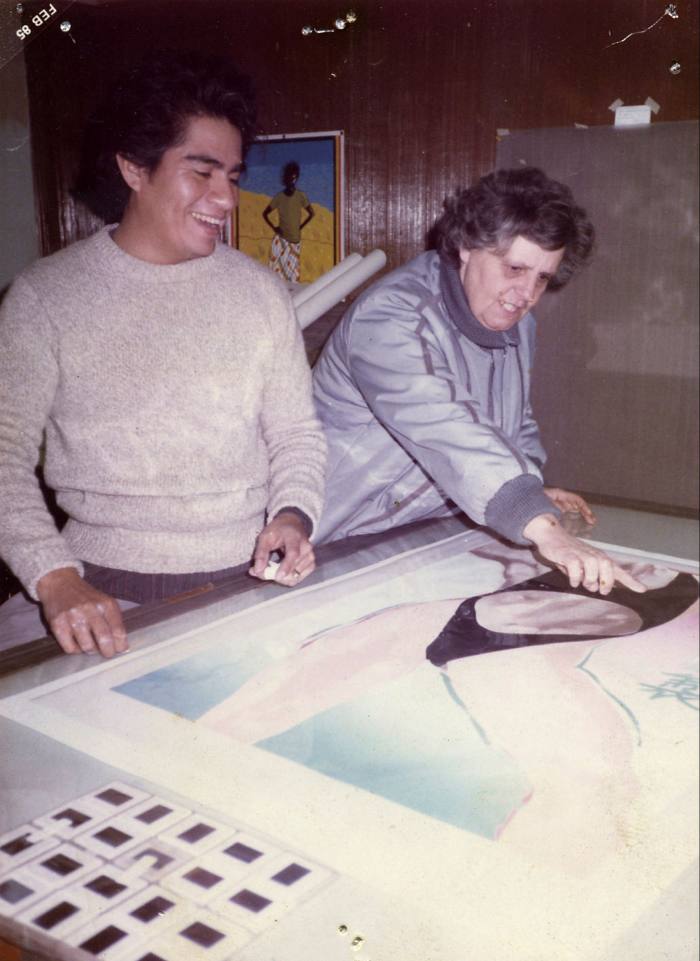 A young man next to an older woman who is pointing at an artwork of a woman in a bikini on a table