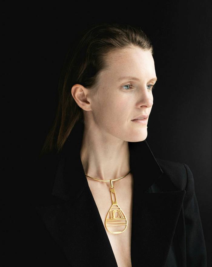 A woman wearing a gold necklace which reminds one of a tennis racket