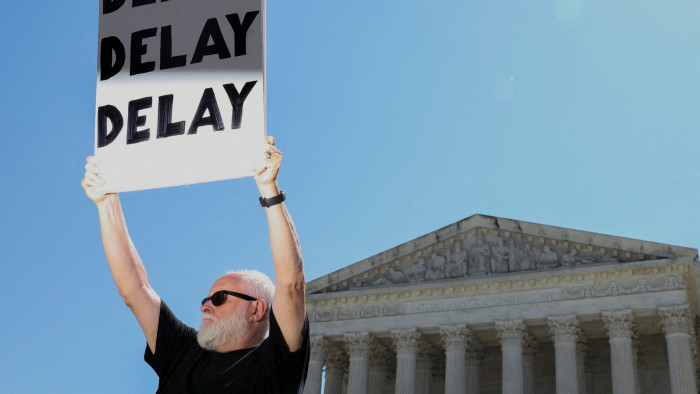 A man holds up a sign saying ‘Delay, Delay, Delay’ outside the US Supreme Court in Washington on June 21 2024