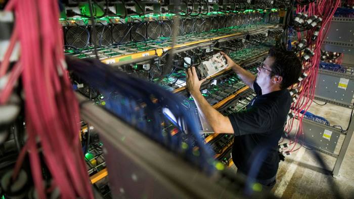 A technician removes a cryptocurrency mining rig from a rack at a Bitfarms facility in Saint-Hyacinthe, Quebec, Canada