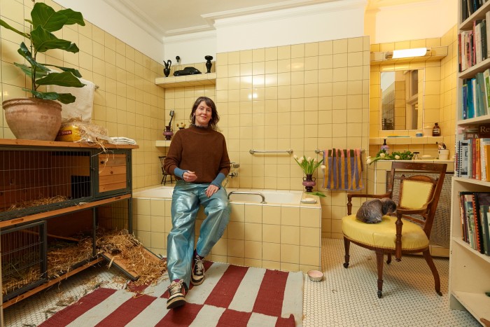 Heath wears her Ganni jeans in the yellow bathroom. Her rabbit Toast sits on the chair