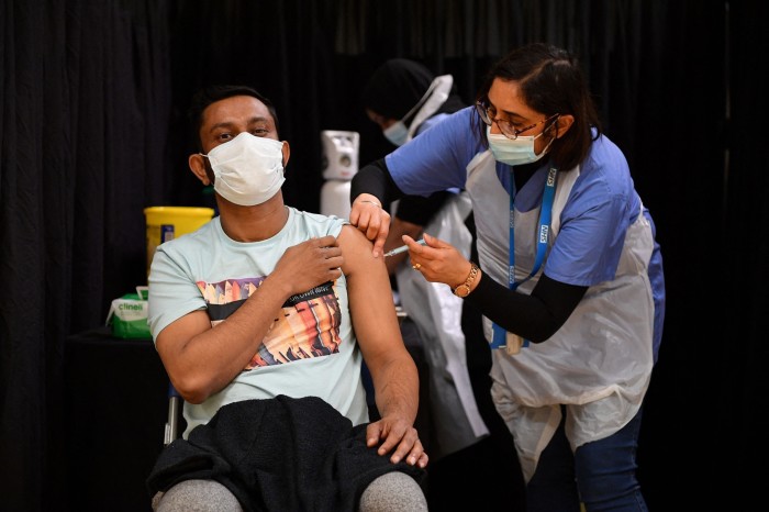 A health worker administers a shot of vaccine to a man in a T-shirt