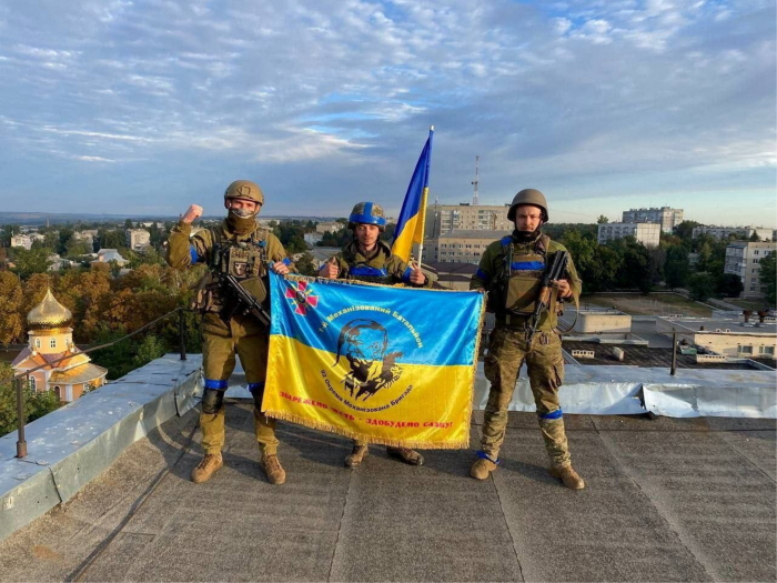 Ukrainian soldiers hold a flag at a rooftop in Kupyansk