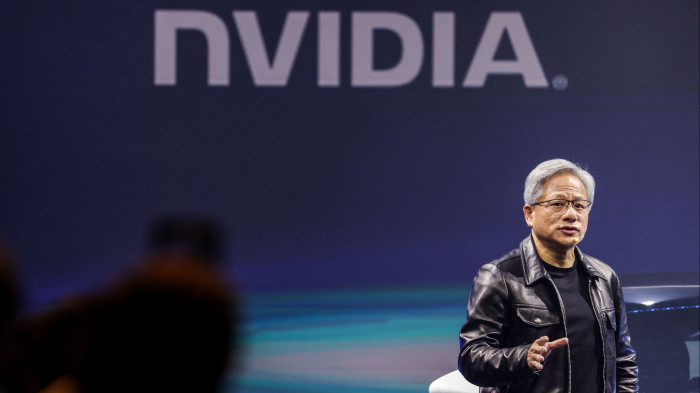 Jensen Huang speaks onstage in his signature leather jacket with the Nvidia logo behind him