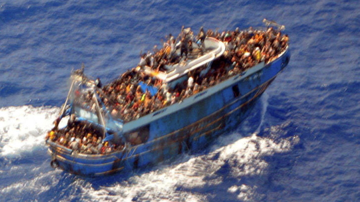 A blue-painted boat heavily crowded with people sails across blue water