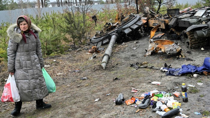 A woman carrying two shopping bags walks past a destroyed Russian army tank near Kyiv