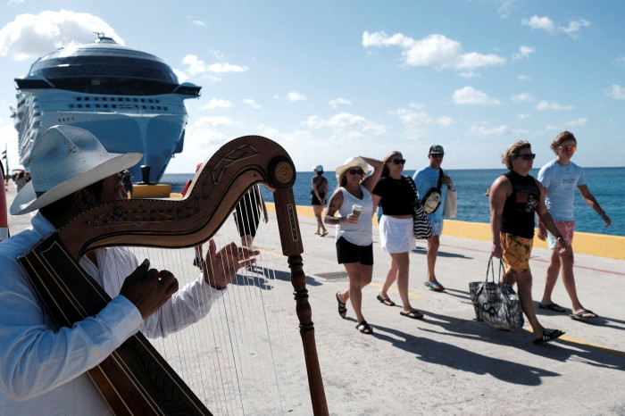 A man plays the harp as tourists leave the Royal Caribbean’s Icon of the Seas