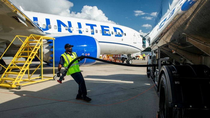 Airport worker pulling a hose from a truck, on a runway with a United Airlines plane in the background